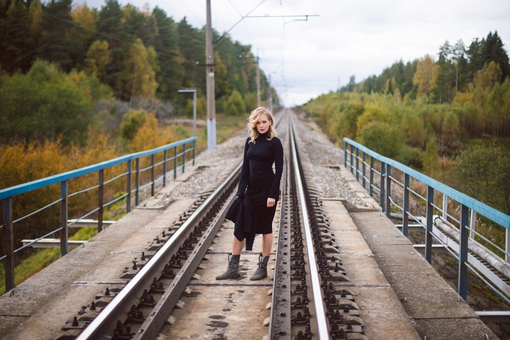 woman in black coat standing on train rail during daytime