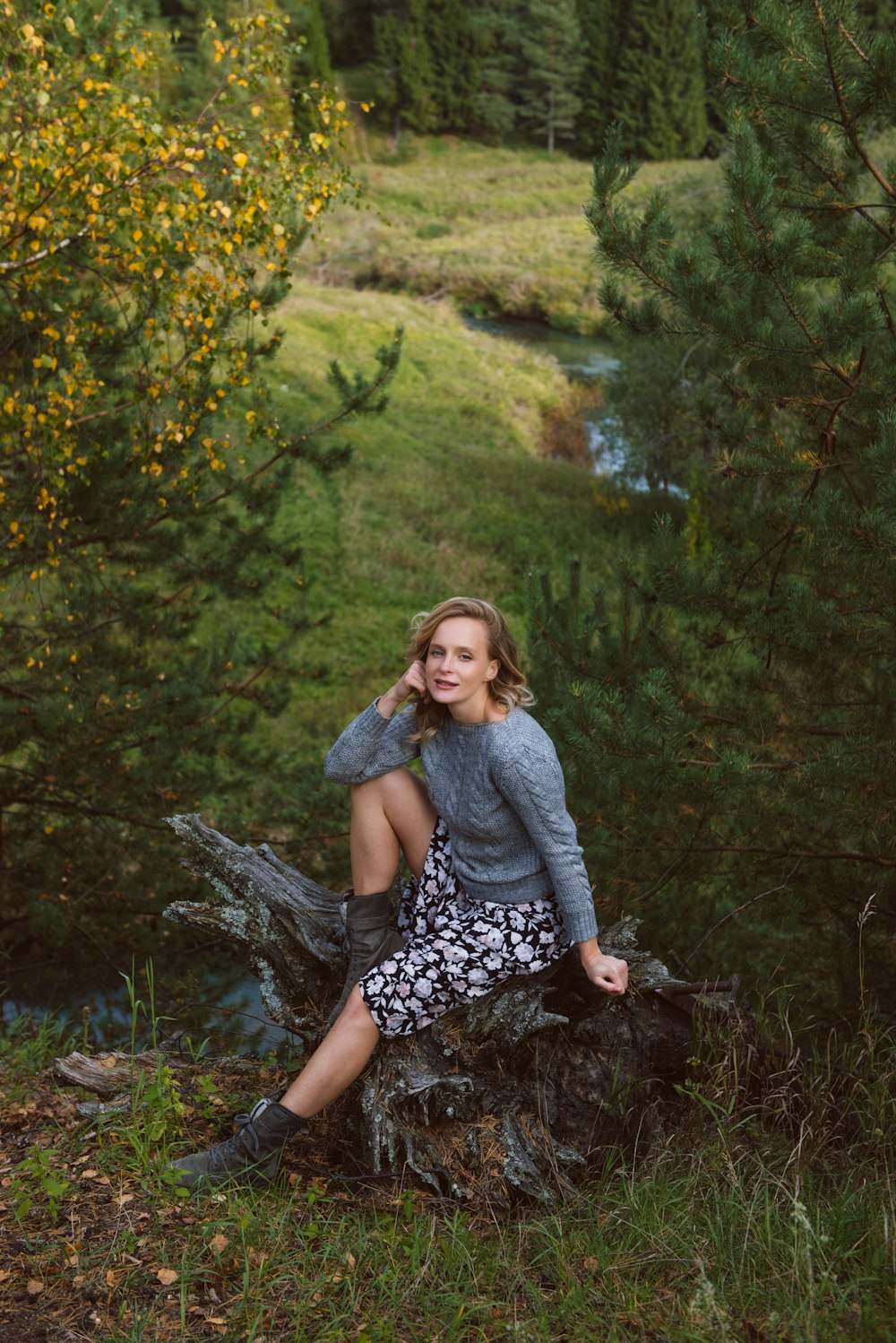 woman in gray sweater and black and white floral skirt sitting on brown rock