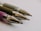 A close-up of four pen tips aligned diagonally on a light background. The pens have metallic tips, and the barrels are partially visible with different colors including purple and gray. The focus is on the pen tips, highlighting their precision and shine.
