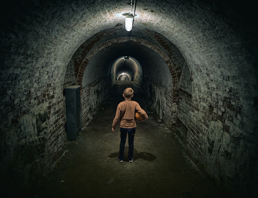 man in brown jacket and black pants standing on tunnel