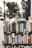 A display of various books arranged on shelves set up outdoors. The books cover a wide range of topics and genres, with titles visible on the spines. The background has a slightly blurred city sidewalk and storefronts, indicative of an urban street setting.