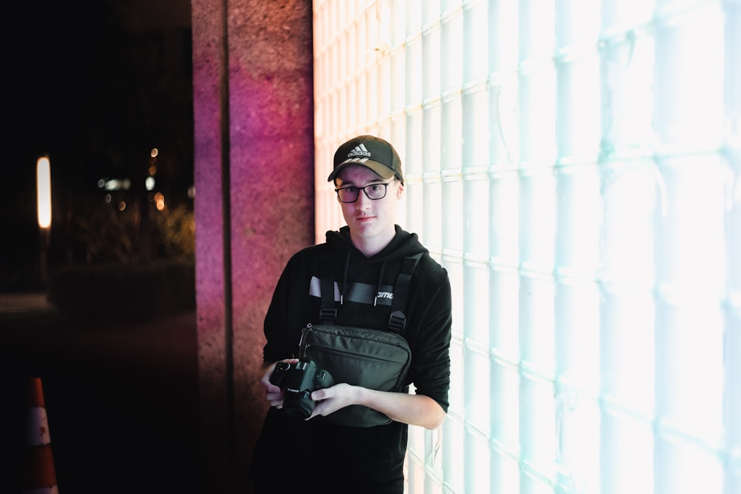 man in black and gray backpack standing beside white wall