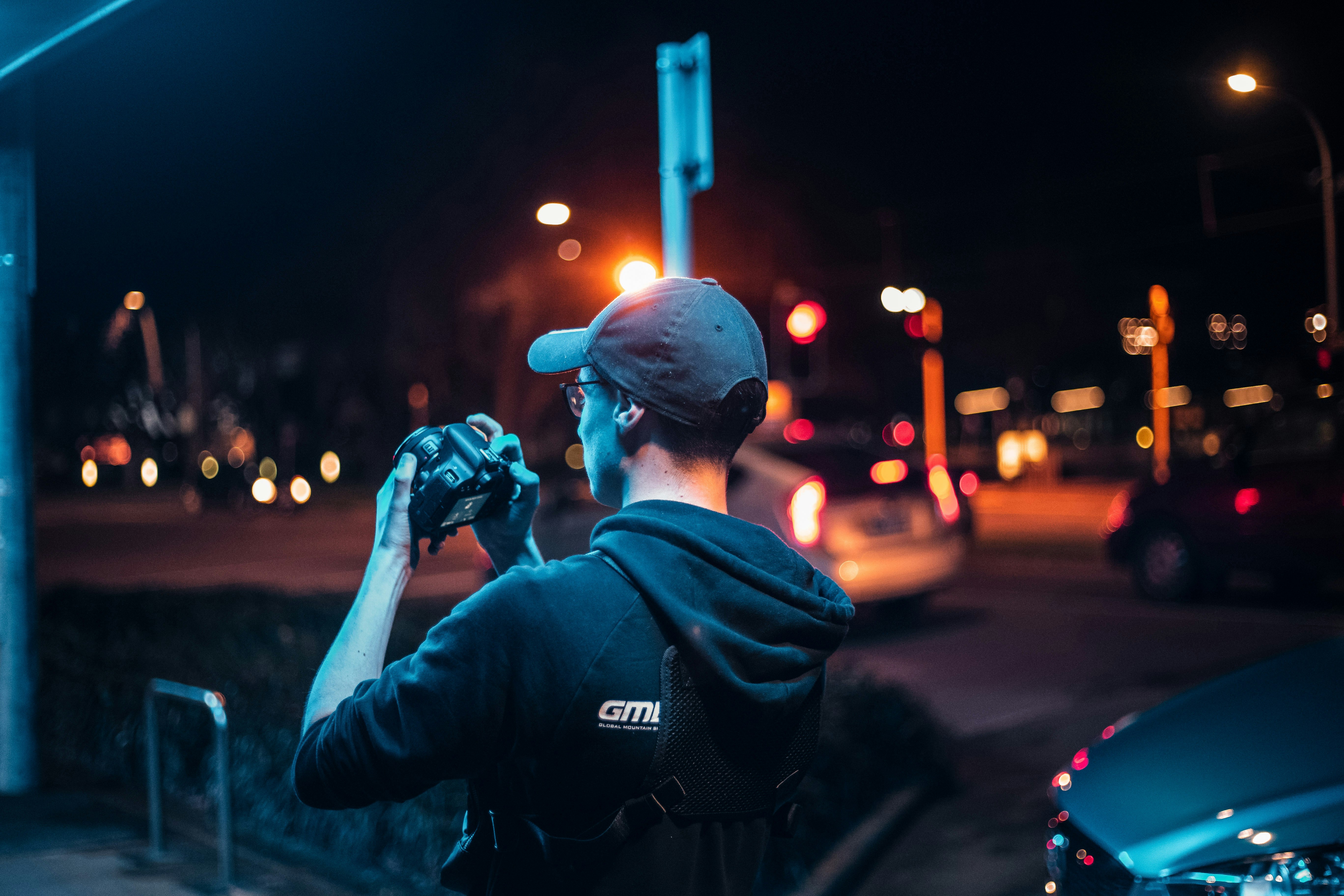man in blue jacket taking photo of city during night time