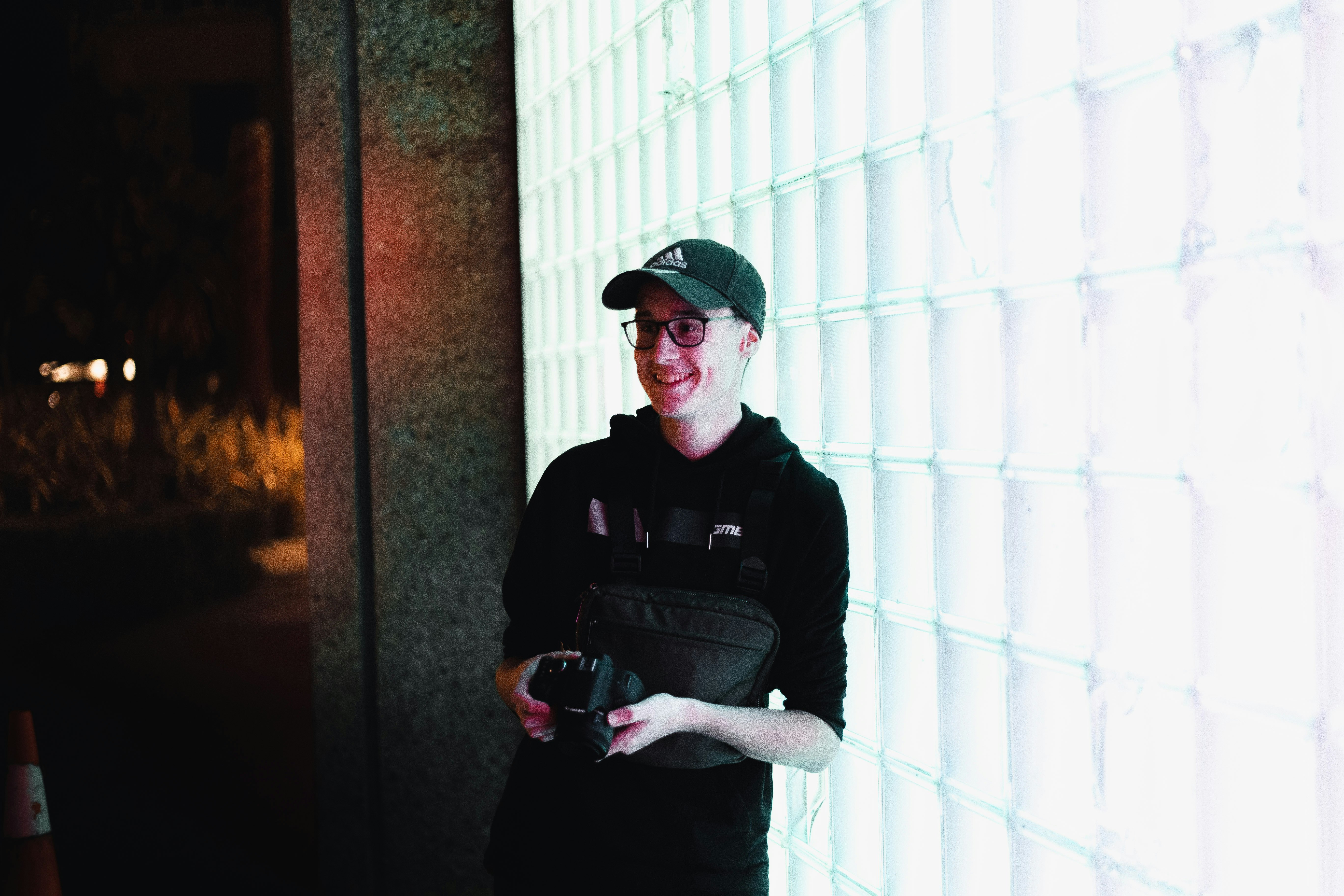 man in black jacket and black cap standing beside white wall