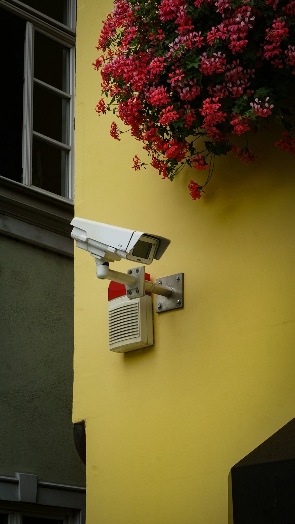 white and gray security camera mounted on yellow painted wall