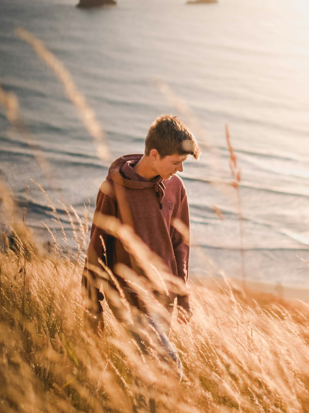 man in red hoodie sitting on brown grass field during daytime