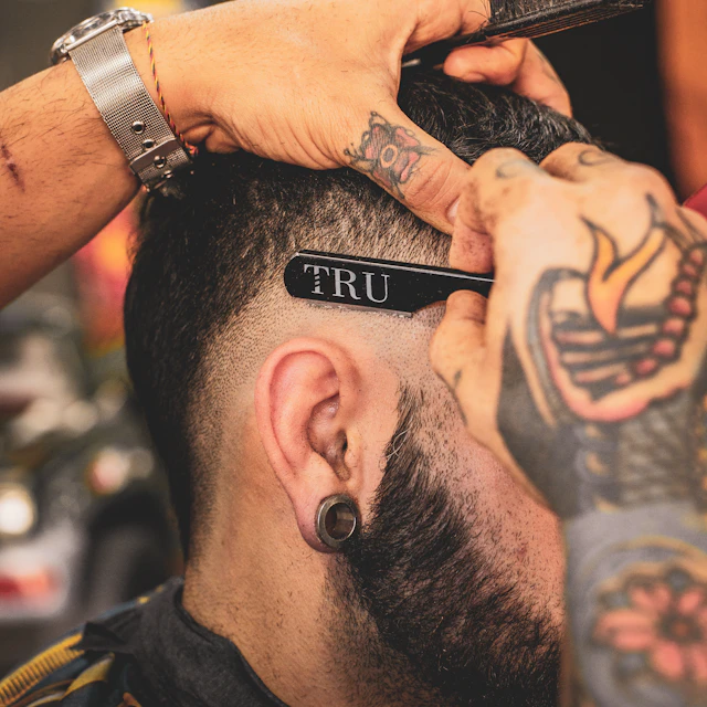 A tattooed barber using a straight razor to trim a man's hair