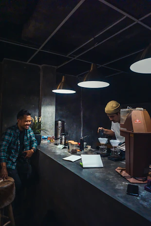 A smiling barista handing over a freshly brewed coffee to a happy customer inside a rustic coffee shop.