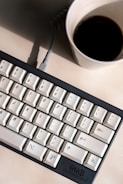 Close-up of hands typing on a mechanical keyboard with coffee nearby.