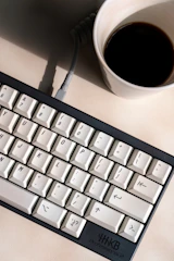 Close-up of hands typing content on a minimalist keyboard with a coffee cup nearby.