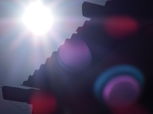 A bright sun shines intensely in the sky, partially blocked by the silhouette of a corrugated roof. Visible lens flare effects create colorful circles and streaks across the image, adding a surreal and dreamy quality.