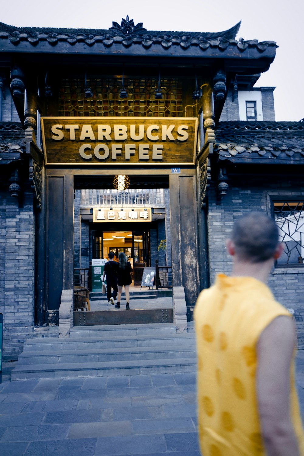 man in white t-shirt walking on sidewalk near building during daytime