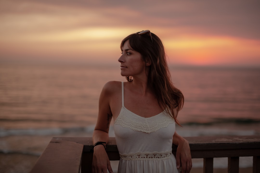 woman in white spaghetti strap dress standing near sea during sunset