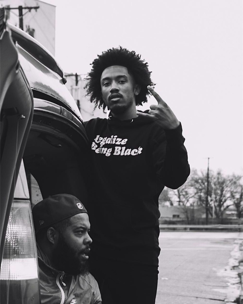 man in black hoodie standing beside car