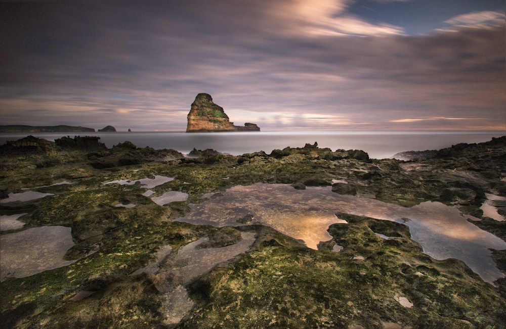 green and brown rock formation on body of water during daytime