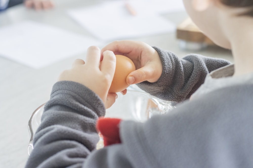 person in gray sweater holding babys hand