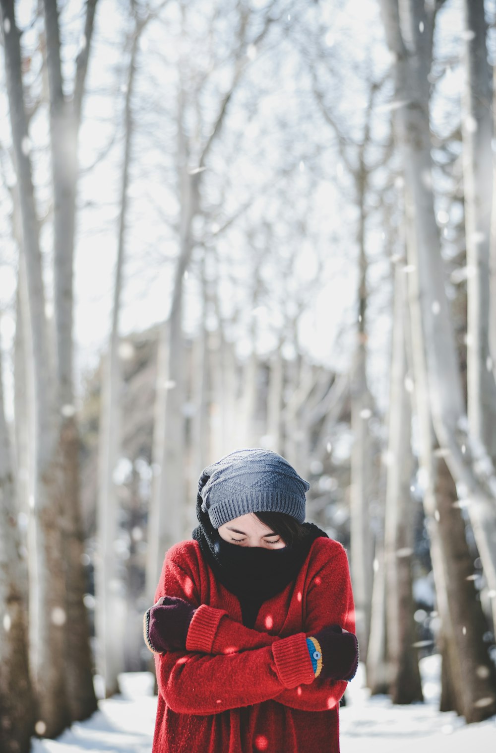 person in red jacket wearing blue knit cap standing near snow covered trees during daytime