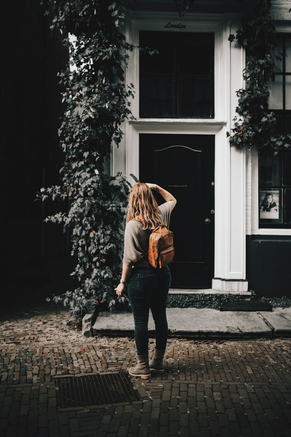 woman in brown jacket and black pants standing near green plant