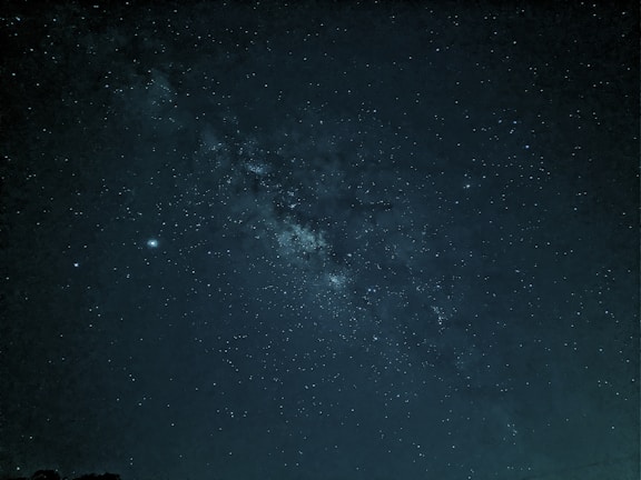 A captivating view of the night sky filled with countless stars and a visible section of the Milky Way galaxy. The dark canvas is dotted with bright star clusters and subtle variations in star brightness, presenting a mesmerizing and vast cosmic panorama.