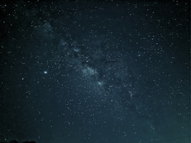 A captivating view of the night sky filled with countless stars and a visible section of the Milky Way galaxy. The dark canvas is dotted with bright star clusters and subtle variations in star brightness, presenting a mesmerizing and vast cosmic panorama.