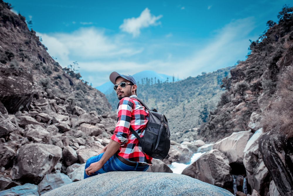 man in black and red plaid shirt and blue denim jeans sitting on rock during daytime