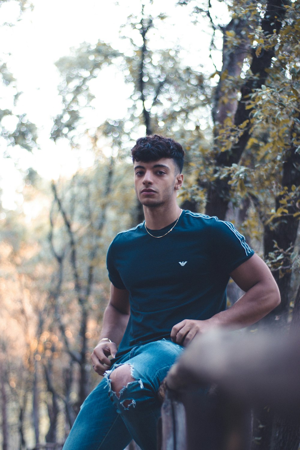 man in blue crew neck t-shirt and blue denim jeans sitting on rock during daytime