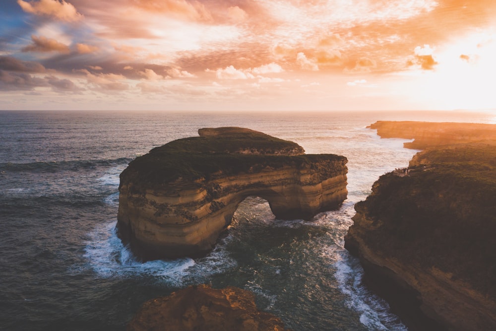 brown rock formation on sea during sunset