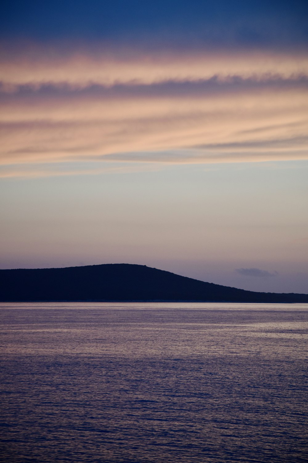 body of water near mountain under cloudy sky during daytime