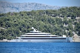 A panoramic view of a Gray Yachts vessel anchored near a rugged coastline with pine trees.