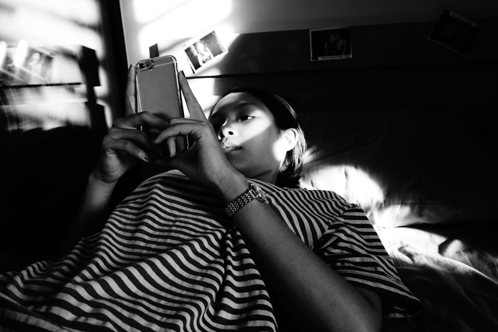 grayscale photo of woman in stripe shirt holding smartphone