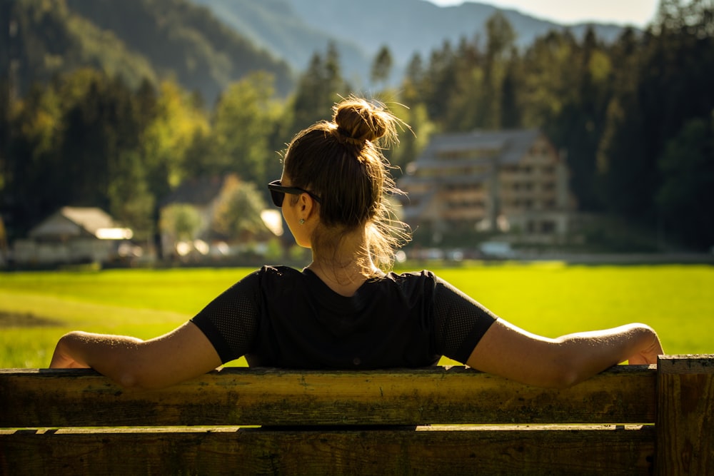 Femme en T-shirt à col rond noir assise sur un banc en bois marron pendant la journée