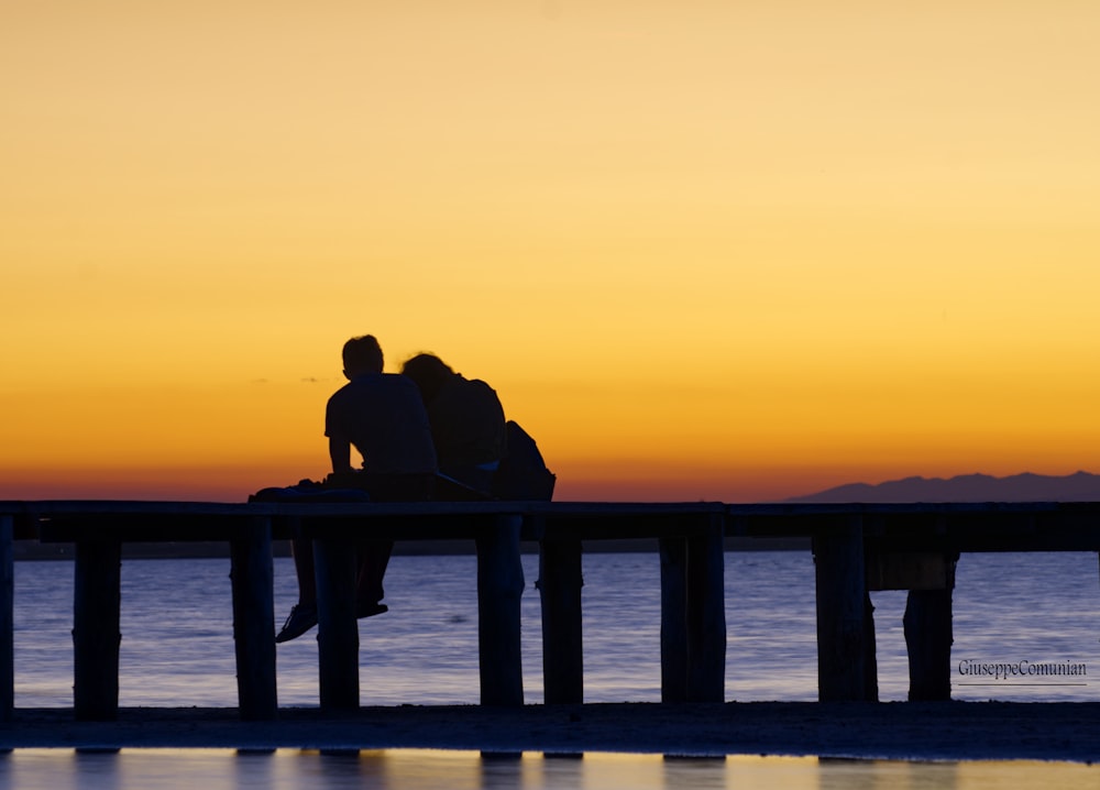 silhouette of couple sitting on bench by the sea during sunset