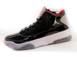 A high-top sneaker with a glossy black finish, featuring mesh panels and red accents on the interior lining. The shoe has a white midsole with a textured pattern and a translucent section on the heel. A distinctive logo is present on the side.