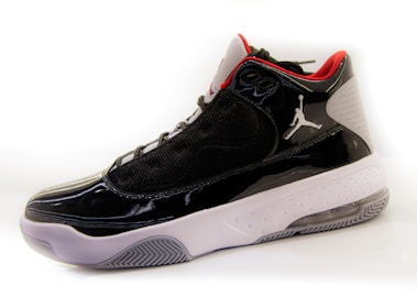 A high-top sneaker with a glossy black finish, featuring mesh panels and red accents on the interior lining. The shoe has a white midsole with a textured pattern and a translucent section on the heel. A distinctive logo is present on the side.