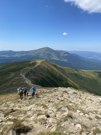 A scenic mountain landscape with travelers hiking along a trail under clear skies.