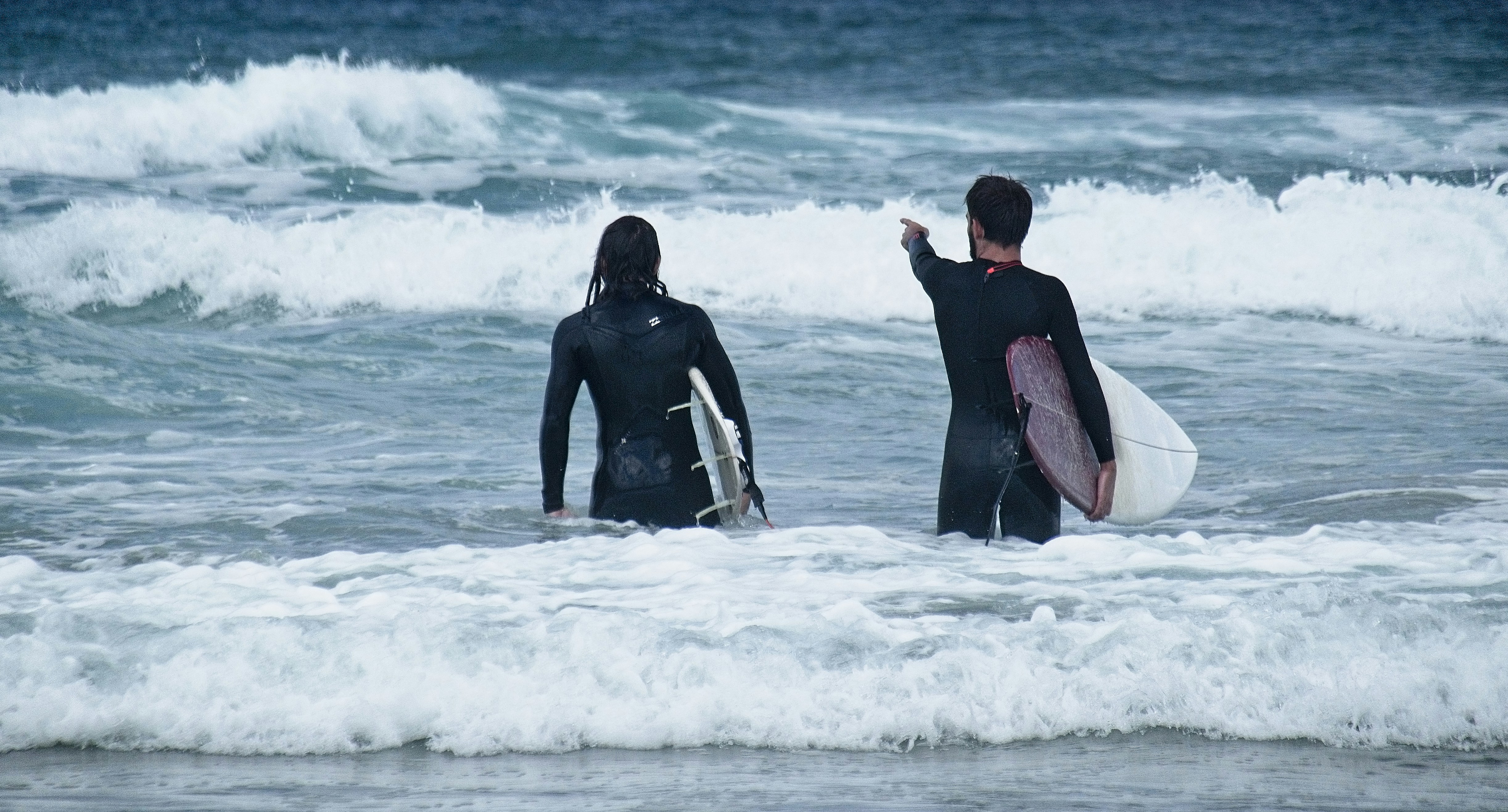 man in black wet suit holding red surfboard on sea waves during daytime