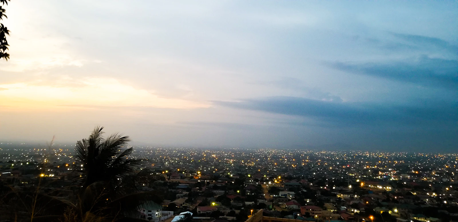 Accra spread out under a wide dusk sky, seen from above the city