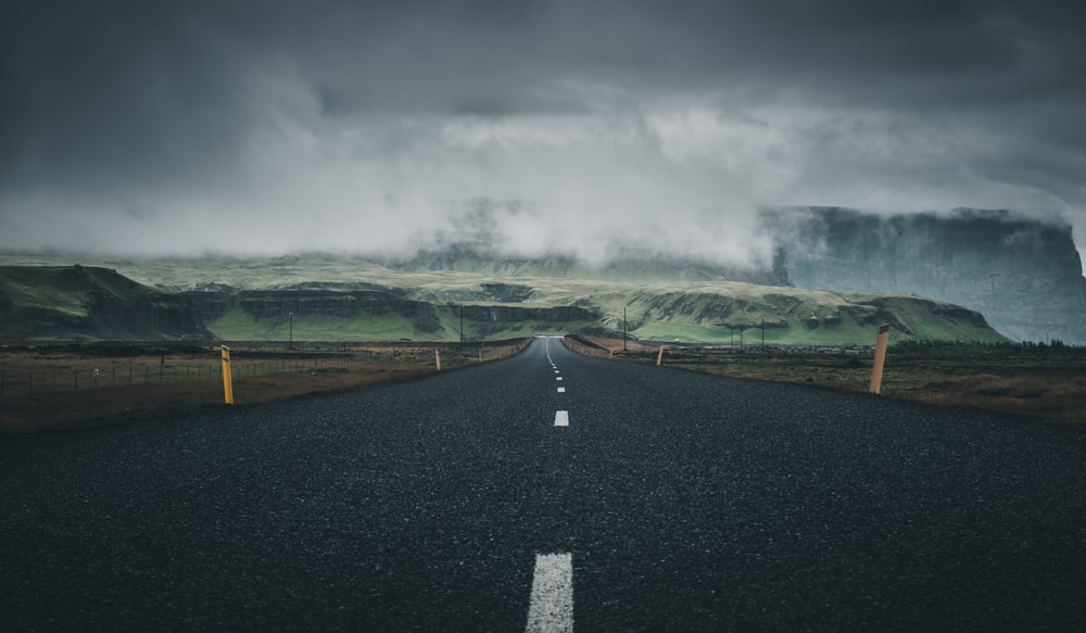 gray concrete road between green grass field under gray clouds