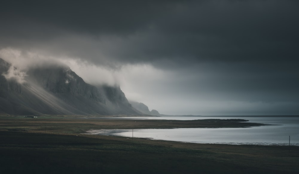 person walking on seashore near mountain under white clouds during daytime