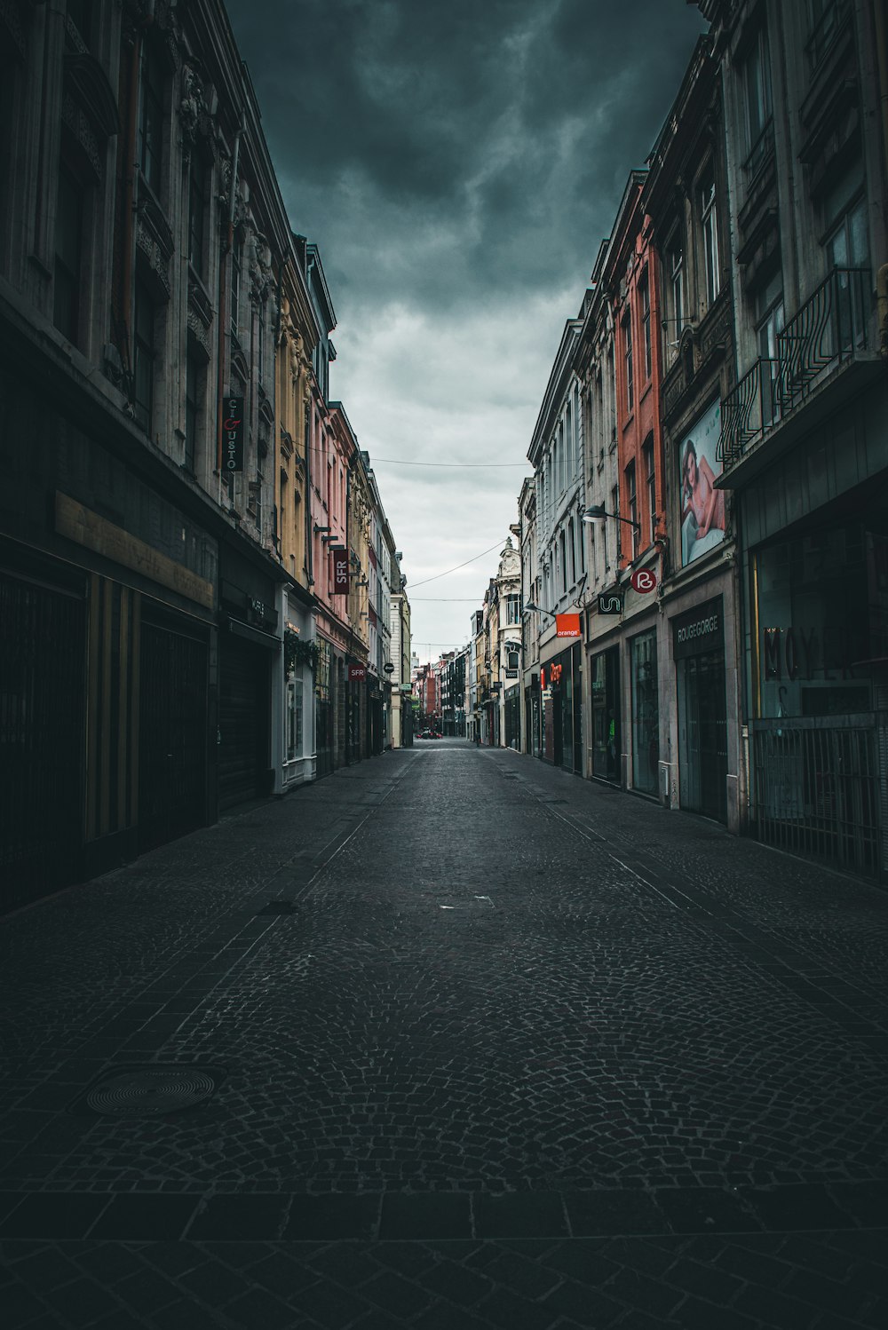 empty road between concrete buildings under white clouds during daytime