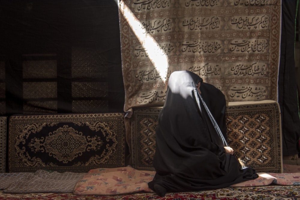 Mujer en hiyab negro sentada en sofá floral marrón y beige