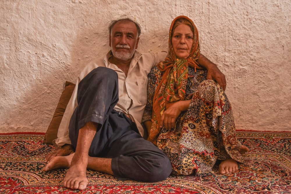 Homme en thobe gris assis à côté d’une femme en robe à fleurs marron et rouge