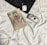 A book titled '44 Charles Street' by Danielle Steel rests on a bed covered with white sheets. Next to the book is a set of wireless earphones and a digital camera. Part of a laptop and a small, square electronic device are also visible.