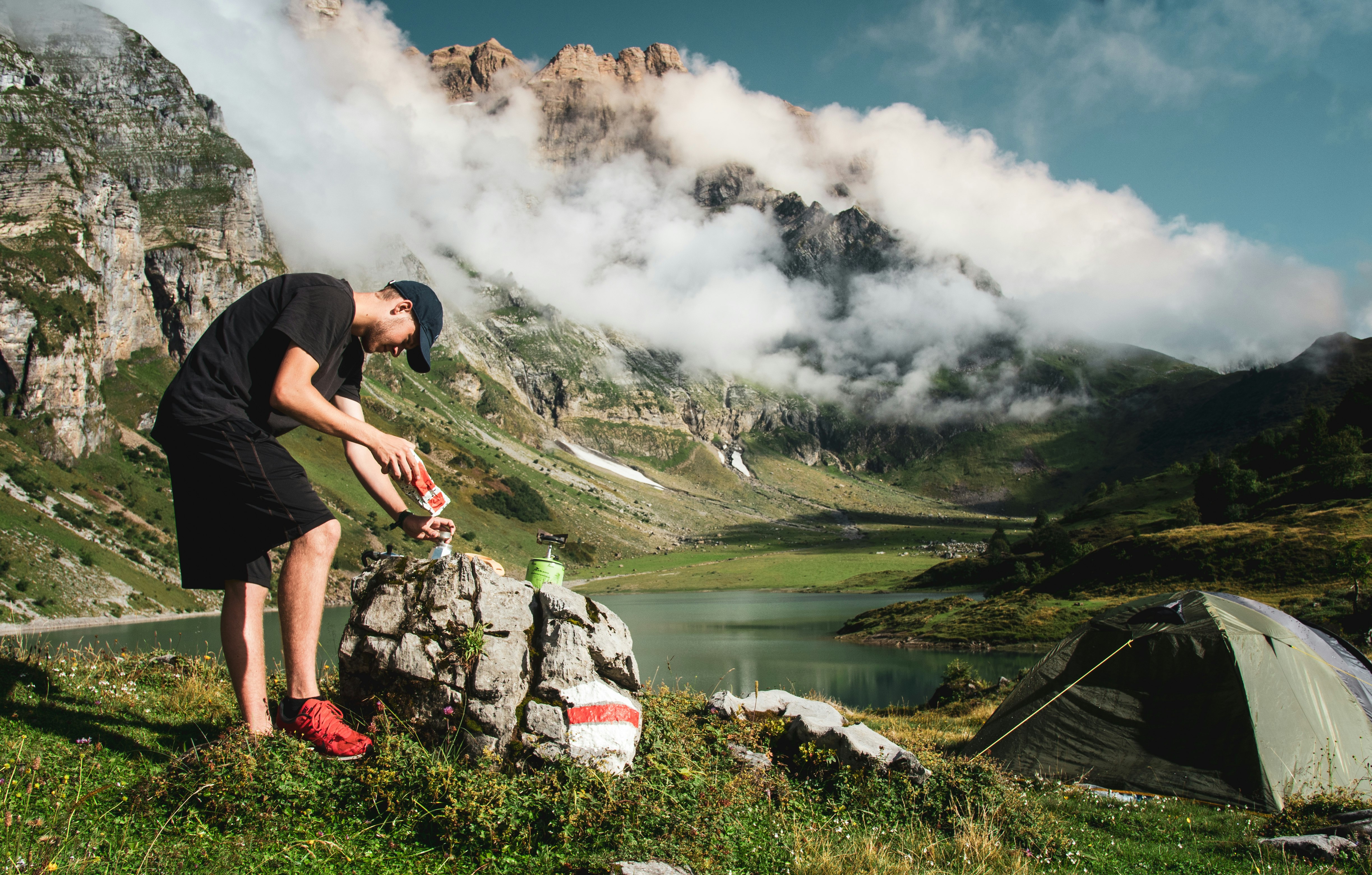 man in black t-shirt and gray shorts standing on rock near lake during daytime