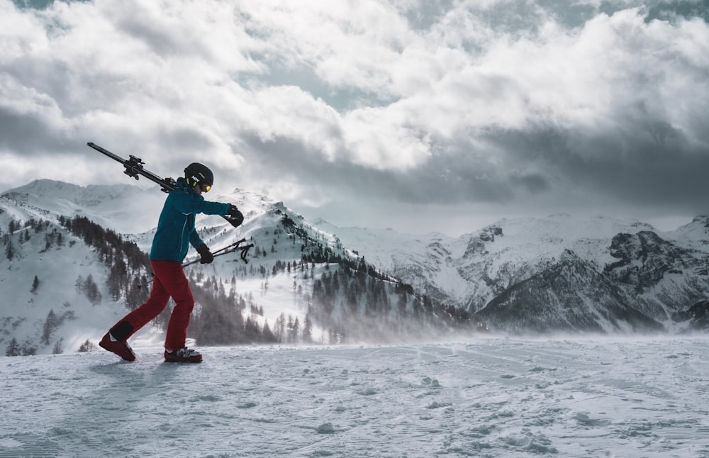 man in blue jacket and red pants standing on snow covered ground