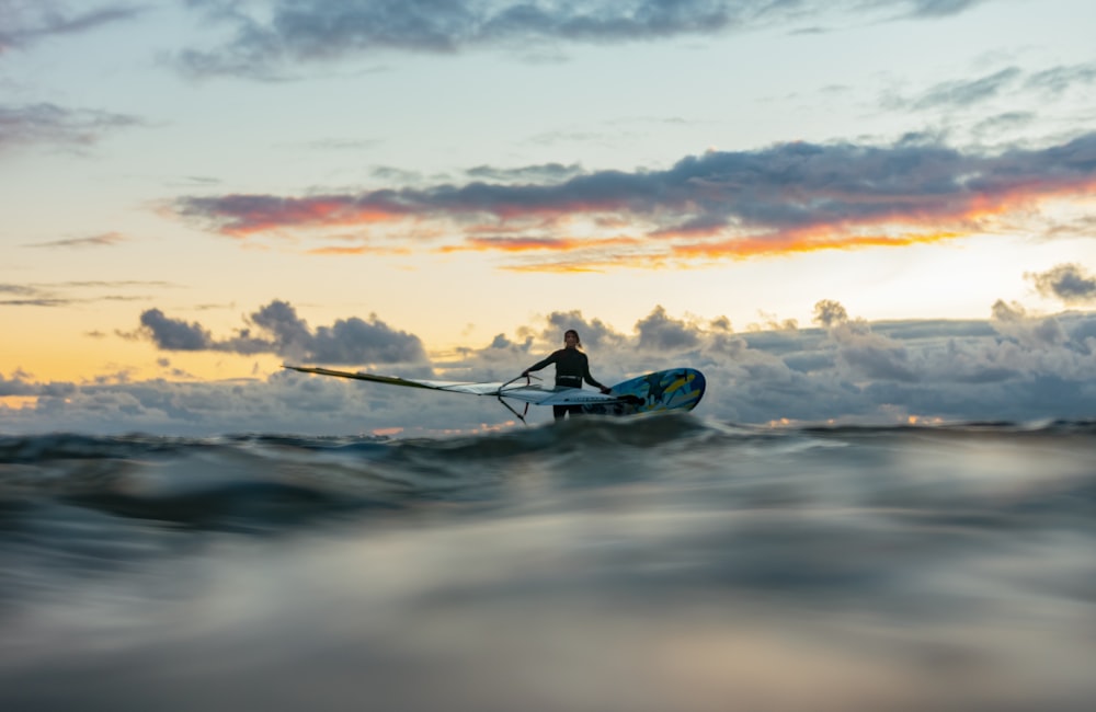 silhouette of man riding on blue kayak on sea during sunset