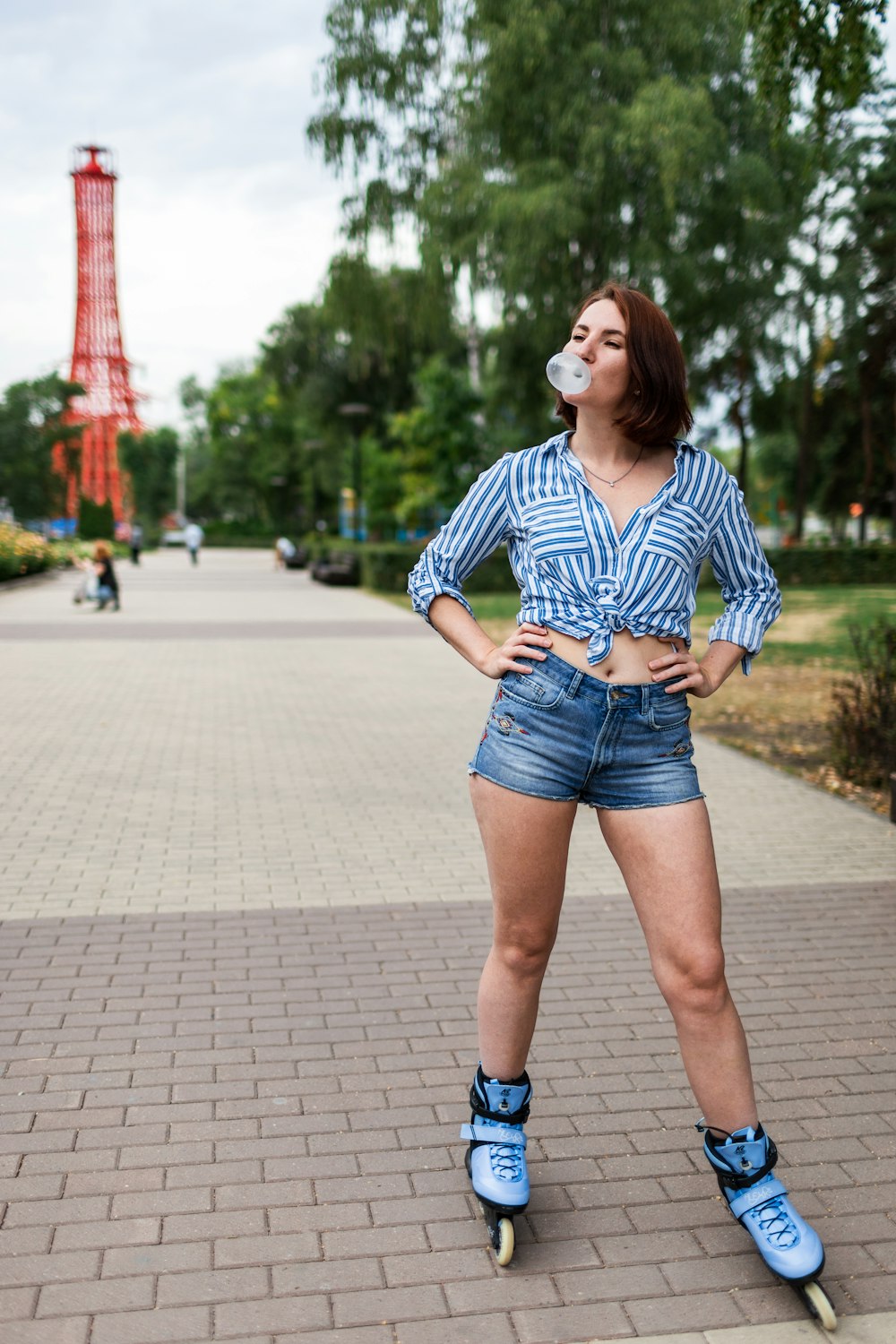 woman in blue and white stripe shirt and blue denim shorts standing on sidewalk during daytime