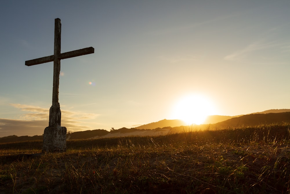 brown cross on green grass field during sunset