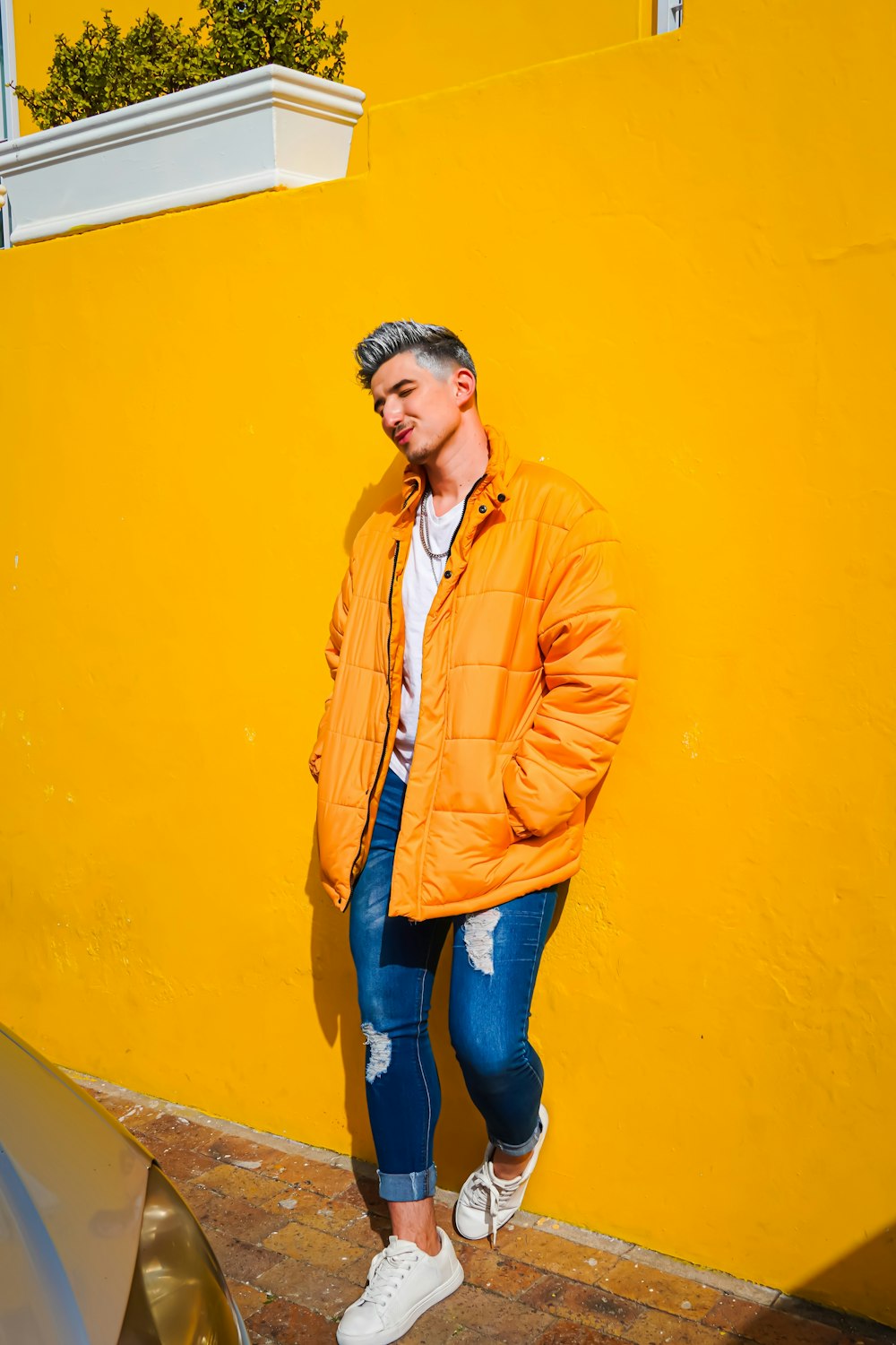 a man in an orange jacket leaning against a yellow wall