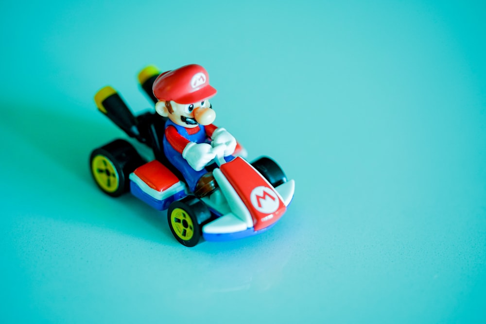 Rothaariger Mann, der rotes und blaues Auto-Plastikspielzeug fährt